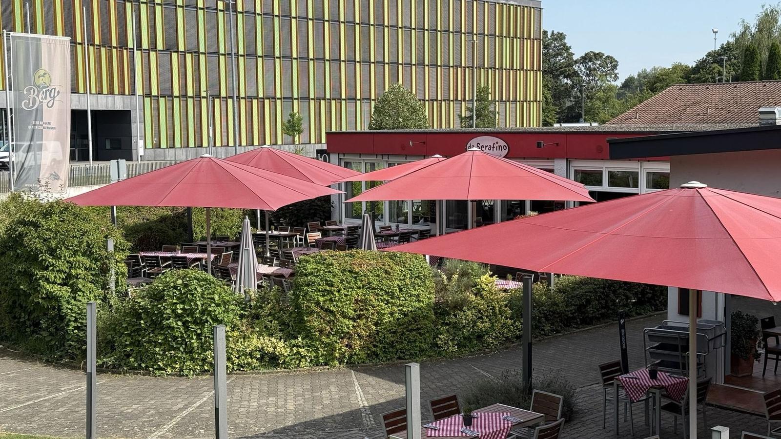 Terrasse von oben mit roten Sonnenschirmen und Grün ringsum